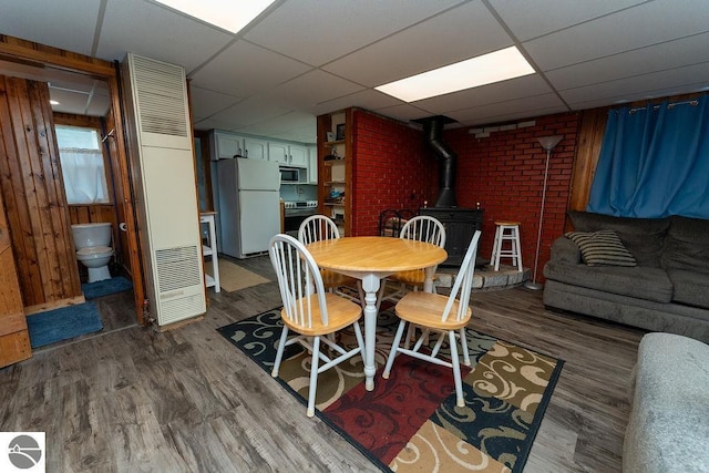 dining area featuring a wood stove, a paneled ceiling, and dark hardwood / wood-style flooring