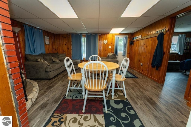 dining area featuring dark wood-type flooring, a paneled ceiling, and wooden walls