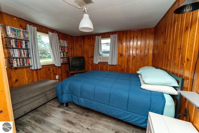 bedroom featuring multiple windows, hardwood / wood-style flooring, and wood walls