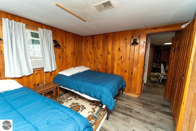 bedroom with hardwood / wood-style floors, wooden walls, and a wood stove