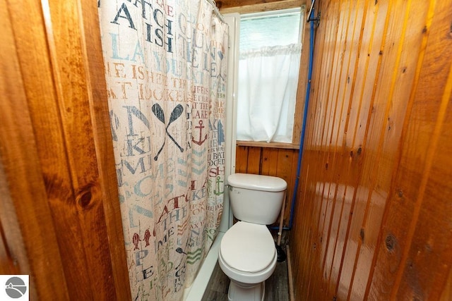 bathroom with a shower with curtain, toilet, and wood walls