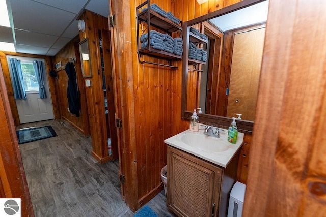 bathroom with wood-type flooring, a drop ceiling, vanity, and wood walls