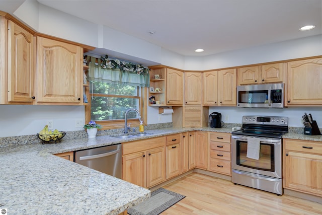 kitchen featuring light stone counters, stainless steel appliances, light brown cabinetry, and sink