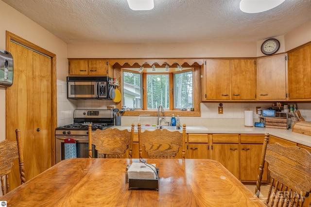 kitchen with a textured ceiling, appliances with stainless steel finishes, brown cabinetry, and backsplash