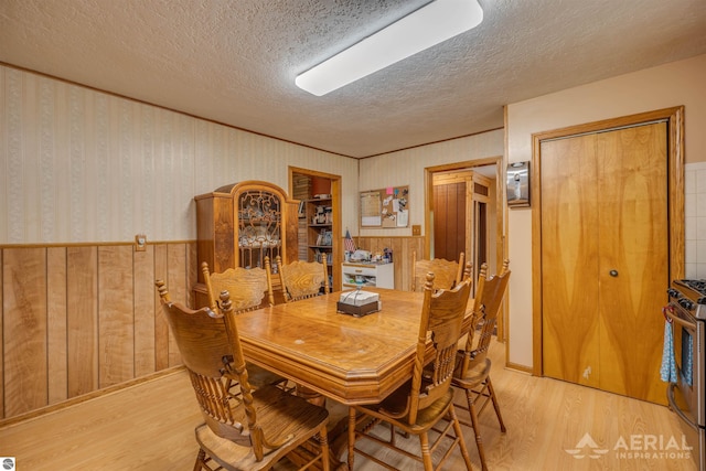 dining room with a wainscoted wall, a textured ceiling, light wood-style flooring, and wallpapered walls