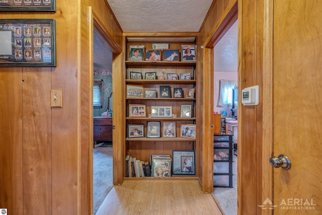 hall with carpet floors, built in shelves, a textured ceiling, and wood finished floors