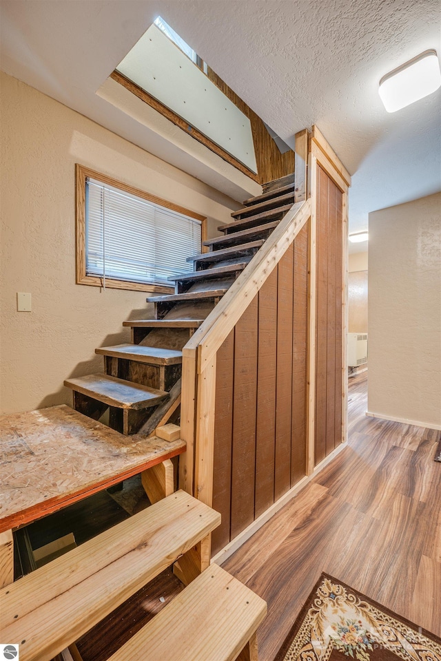 staircase featuring a textured ceiling, a textured wall, and wood finished floors