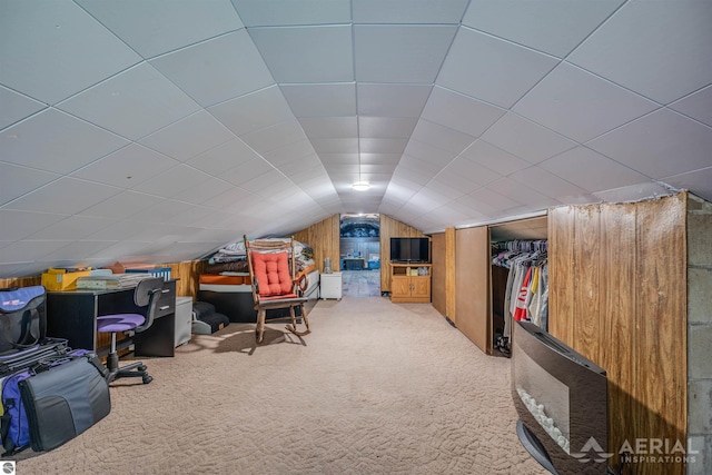 carpeted office featuring vaulted ceiling and wood walls