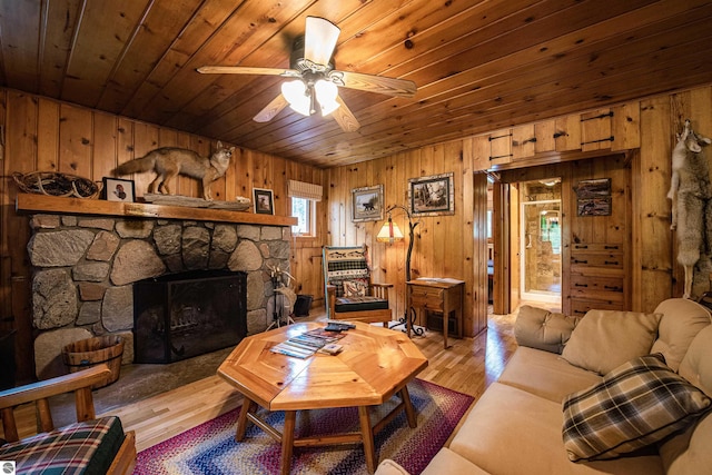 living room with wooden ceiling, a stone fireplace, hardwood / wood-style flooring, ceiling fan, and wood walls