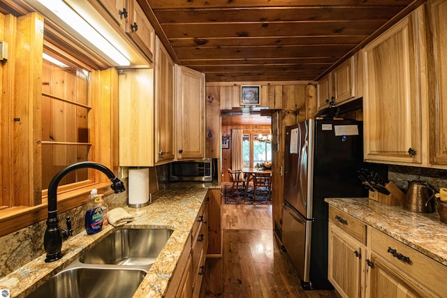 kitchen featuring wooden walls, stainless steel appliances, light stone counters, sink, and dark wood-type flooring