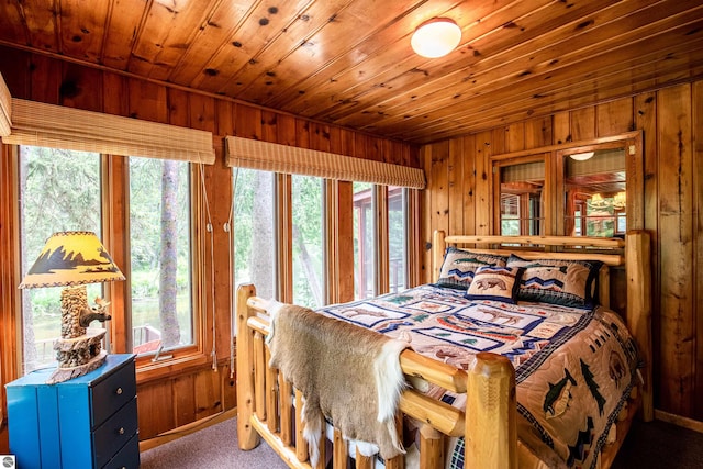 carpeted bedroom with wooden walls, wood ceiling, and multiple windows