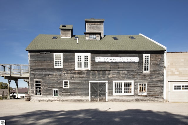 rear view of property featuring a shingled roof and a chimney