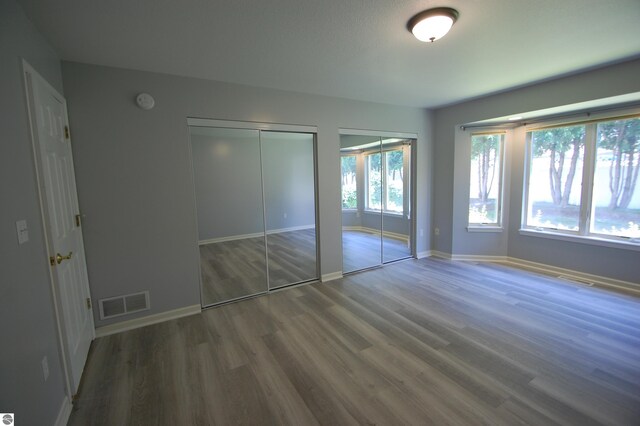 unfurnished bedroom featuring wood-type flooring and multiple closets