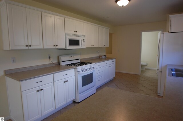 kitchen with light tile patterned floors, white appliances, sink, and white cabinetry