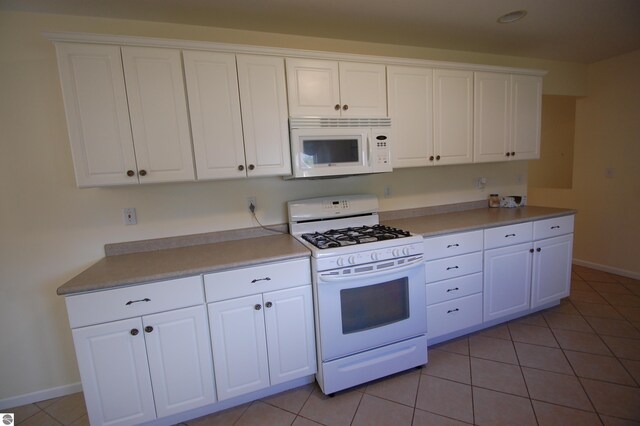 kitchen with white appliances, light tile patterned flooring, and white cabinetry