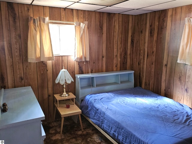 bedroom with a drop ceiling, wood walls, and dark carpet