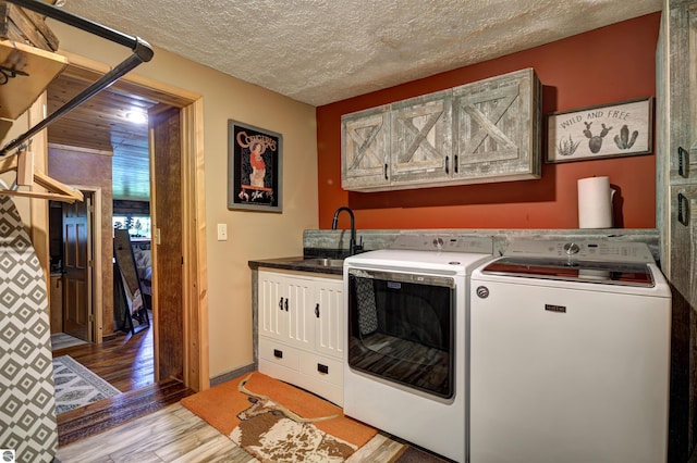 clothes washing area with sink, light hardwood / wood-style flooring, independent washer and dryer, cabinets, and a textured ceiling