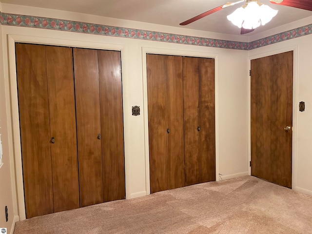 unfurnished bedroom featuring ceiling fan, two closets, and carpet flooring