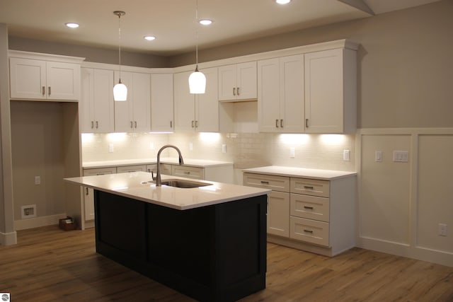 kitchen featuring backsplash, a center island with sink, wood finished floors, white cabinetry, and a sink