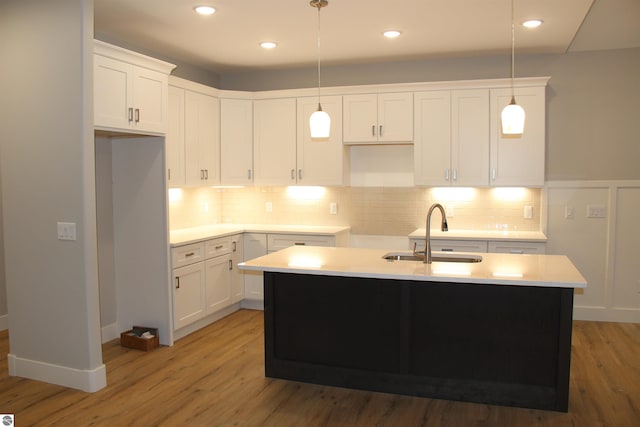 kitchen with a sink, backsplash, light wood-style floors, and an island with sink