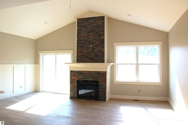 unfurnished living room with visible vents, light wood-type flooring, wainscoting, a fireplace, and high vaulted ceiling