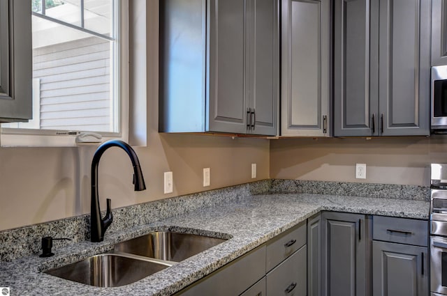 kitchen with light stone countertops, sink, stainless steel microwave, and gray cabinetry