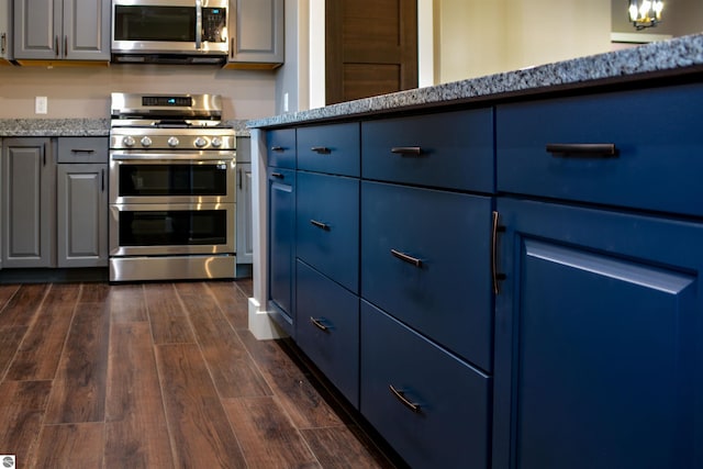 kitchen with appliances with stainless steel finishes, dark wood-type flooring, blue cabinetry, and light stone countertops