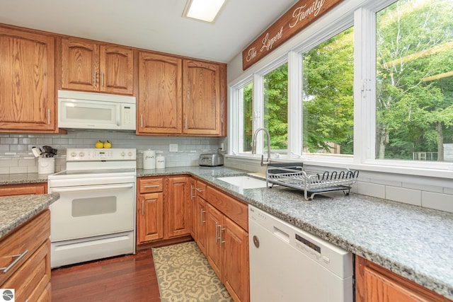 kitchen featuring decorative backsplash, light stone counters, dark wood-type flooring, white appliances, and sink