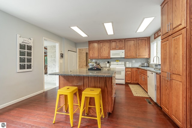 kitchen featuring white appliances, sink, dark wood-type flooring, and a kitchen bar