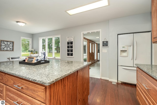 kitchen with white refrigerator with ice dispenser, dark hardwood / wood-style flooring, a kitchen island, and light stone countertops