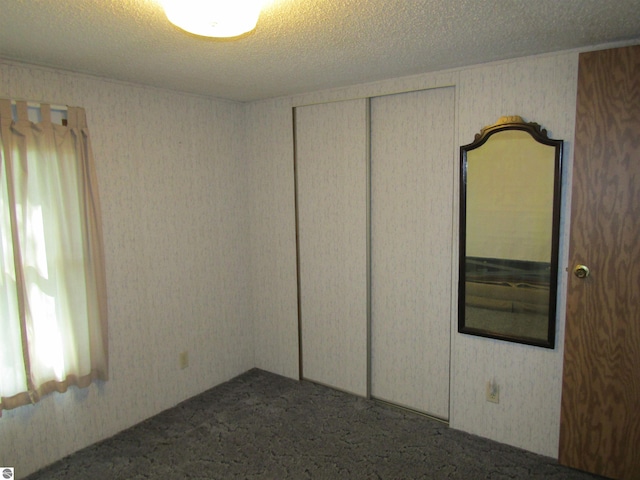 unfurnished room featuring a textured ceiling, dark colored carpet, and wallpapered walls