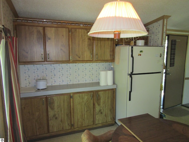 kitchen featuring brown cabinets, freestanding refrigerator, light countertops, and wallpapered walls