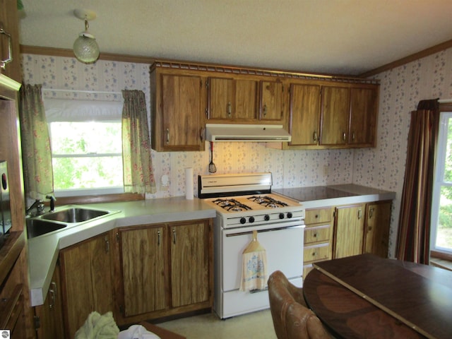 kitchen featuring light countertops, brown cabinetry, white range with gas cooktop, under cabinet range hood, and wallpapered walls