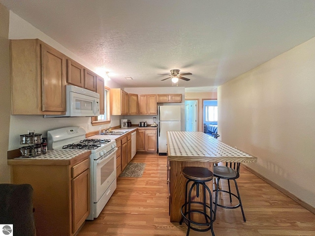 kitchen featuring white appliances, a healthy amount of sunlight, a breakfast bar, and light hardwood / wood-style floors