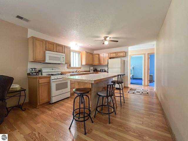 kitchen with a kitchen island, a breakfast bar, ceiling fan, white appliances, and light hardwood / wood-style flooring