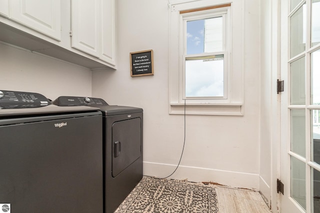 clothes washing area featuring light hardwood / wood-style flooring, washing machine and dryer, and cabinets