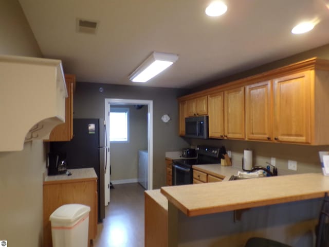 kitchen with sink, black electric range, a breakfast bar area, kitchen peninsula, and fridge