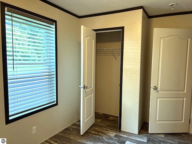 unfurnished bedroom featuring ornamental molding, a closet, a textured ceiling, and dark wood-style floors