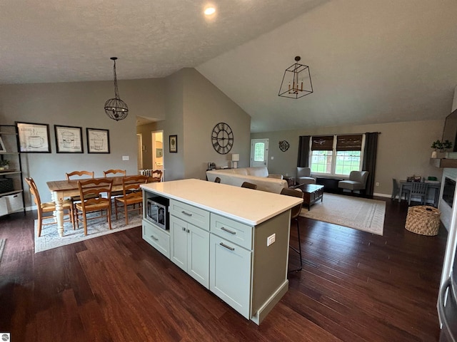 kitchen featuring stainless steel microwave, dark wood-type flooring, a kitchen island, and lofted ceiling