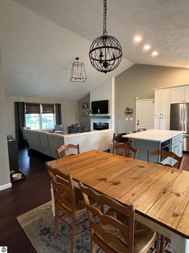 dining space with a textured ceiling, a notable chandelier, dark wood-type flooring, and lofted ceiling