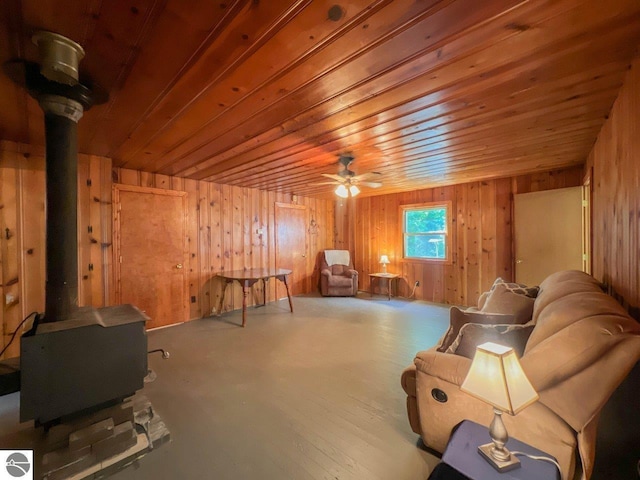 living area featuring a ceiling fan, wooden ceiling, a wood stove, and wooden walls