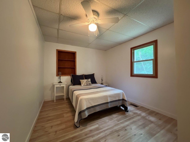 bedroom with light wood finished floors, visible vents, baseboards, and a drop ceiling