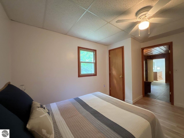 bedroom featuring a drop ceiling, ceiling fan, baseboards, and wood finished floors