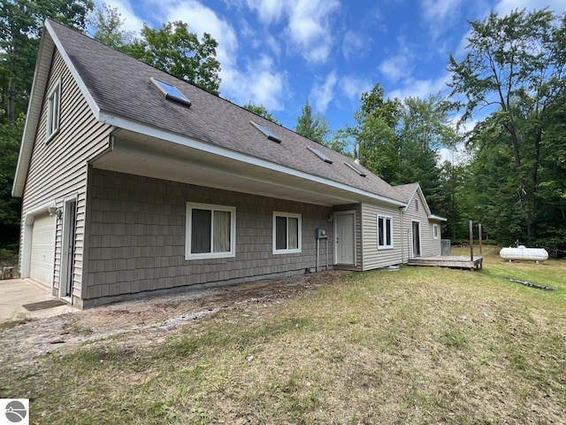 rear view of house featuring roof with shingles, a lawn, a wooden deck, and an attached garage