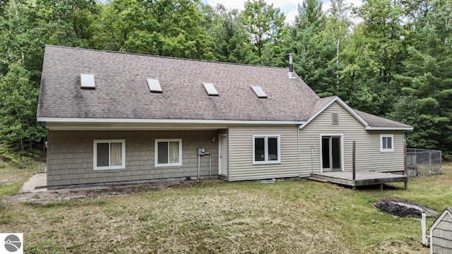 back of house with a deck, a yard, roof with shingles, and fence