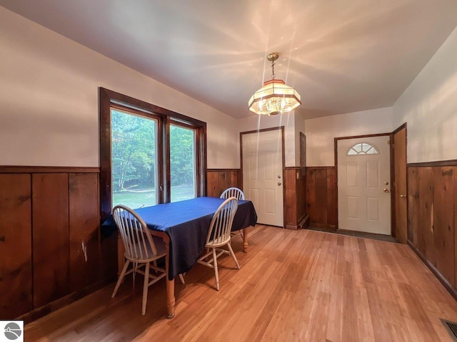 dining space with light wood-type flooring, wood walls, wainscoting, and visible vents