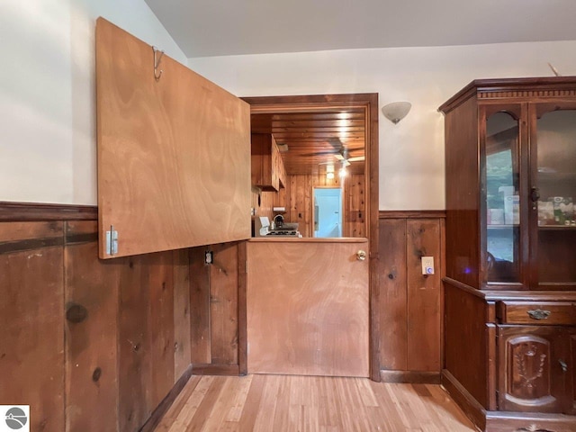 kitchen with a wainscoted wall, light wood finished floors, wood walls, and glass insert cabinets