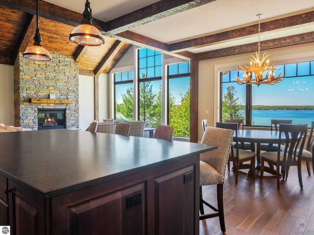 kitchen with vaulted ceiling with beams, dark brown cabinetry, a stone fireplace, dark hardwood / wood-style flooring, and a water view