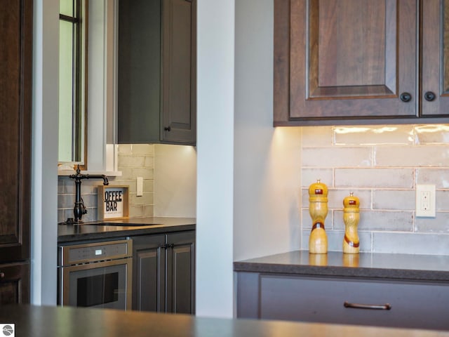 11305 Evergreen, Charlevoix, MI 49720 - kitchen with stainless steel oven, tasteful backsplash, dark brown cabinetry, and dark countertops
