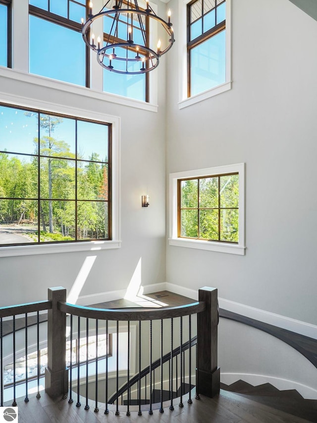 staircase with a chandelier, a high ceiling, hardwood / wood-style flooring, and a healthy amount of sunlight